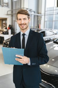Confident car salesman with clipboard in a modern dealership showroom