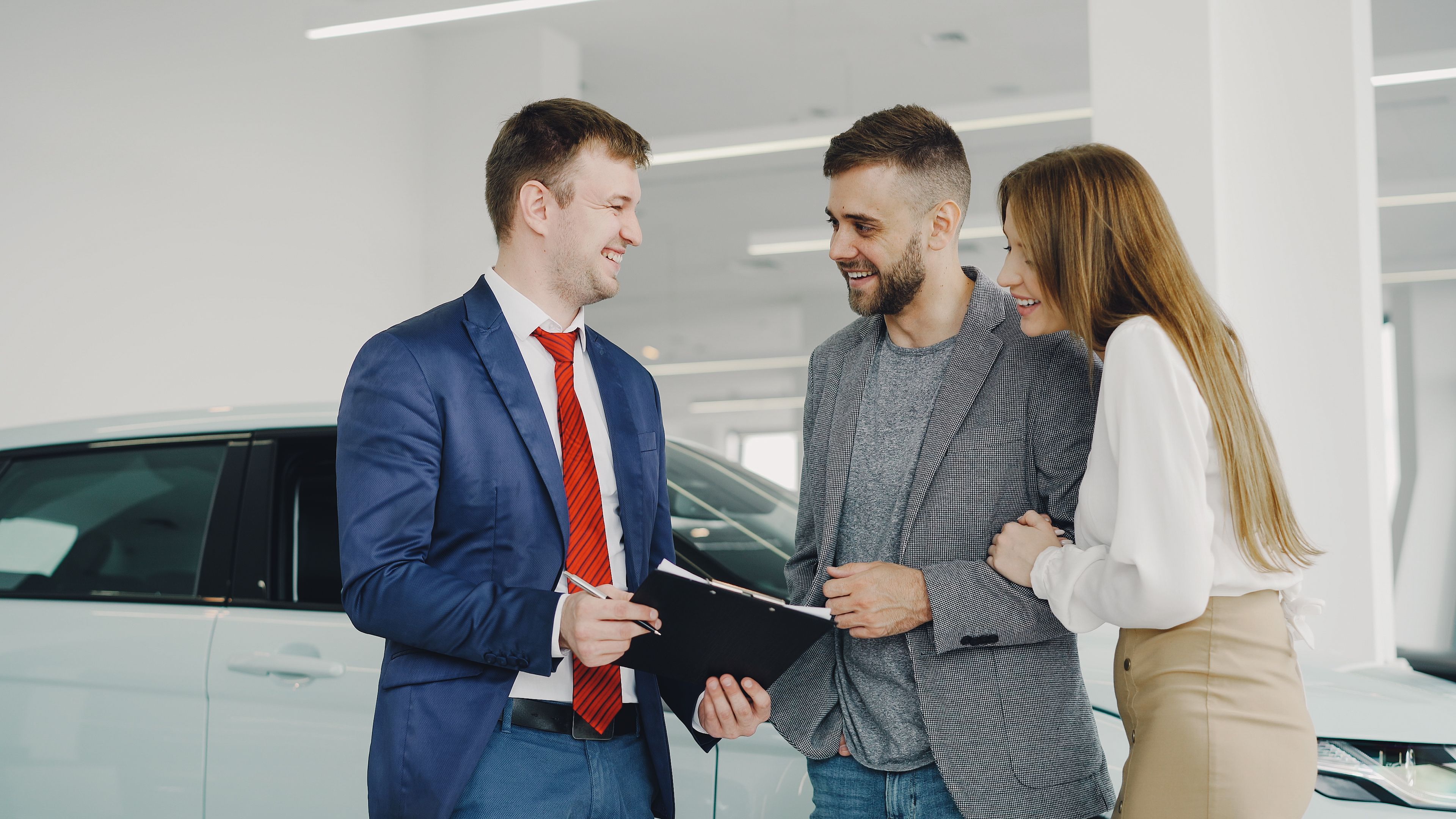 Smiling couple buying a car from a confident salesman in a modern dealership